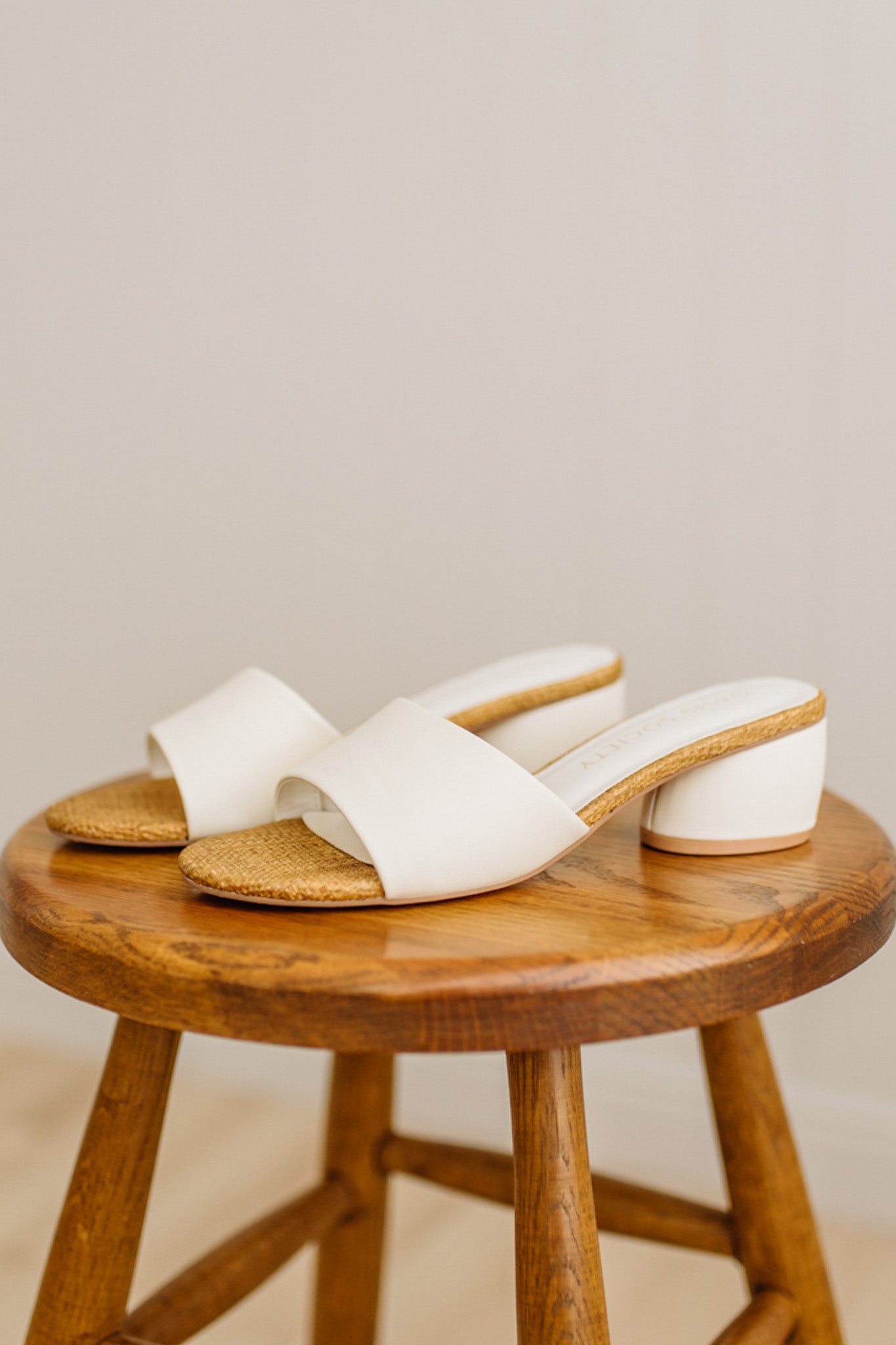 White sandals with wooden sole on a wooden stool against a beige background