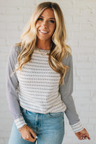 Woman wearing a striped long-sleeve top and jeans against a white brick wall.
