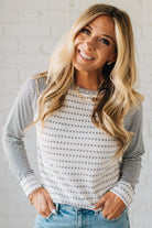 Woman wearing a striped long-sleeve top and jeans against a white brick wall.
