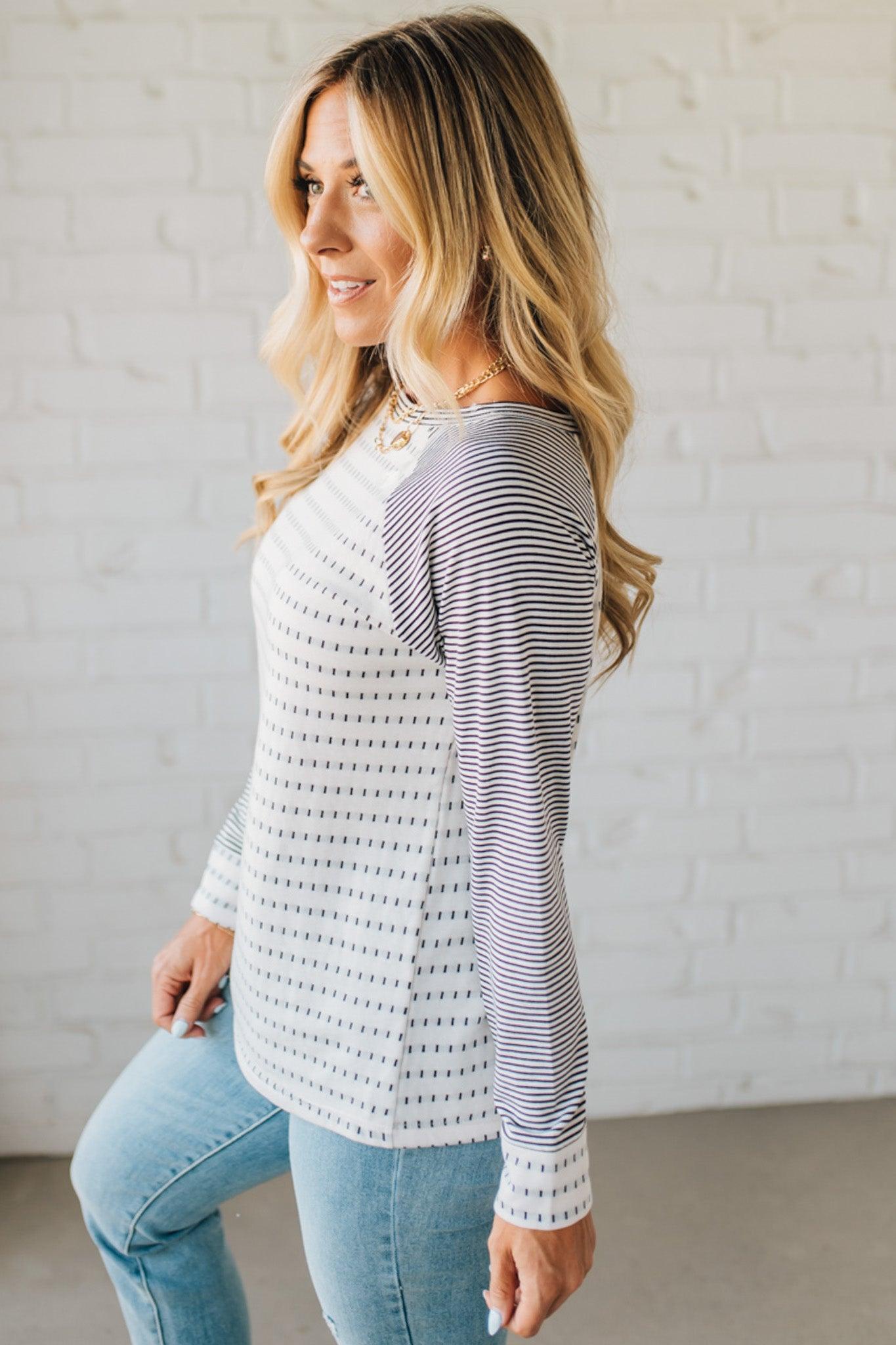 Woman wearing a striped long-sleeve top and jeans against a white brick wall.