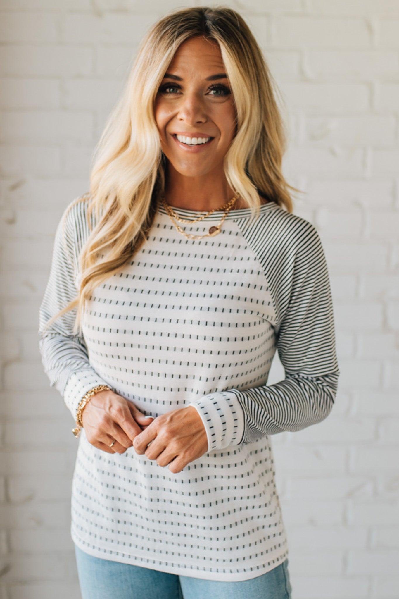 Woman wearing a striped sweater against a white brick wall