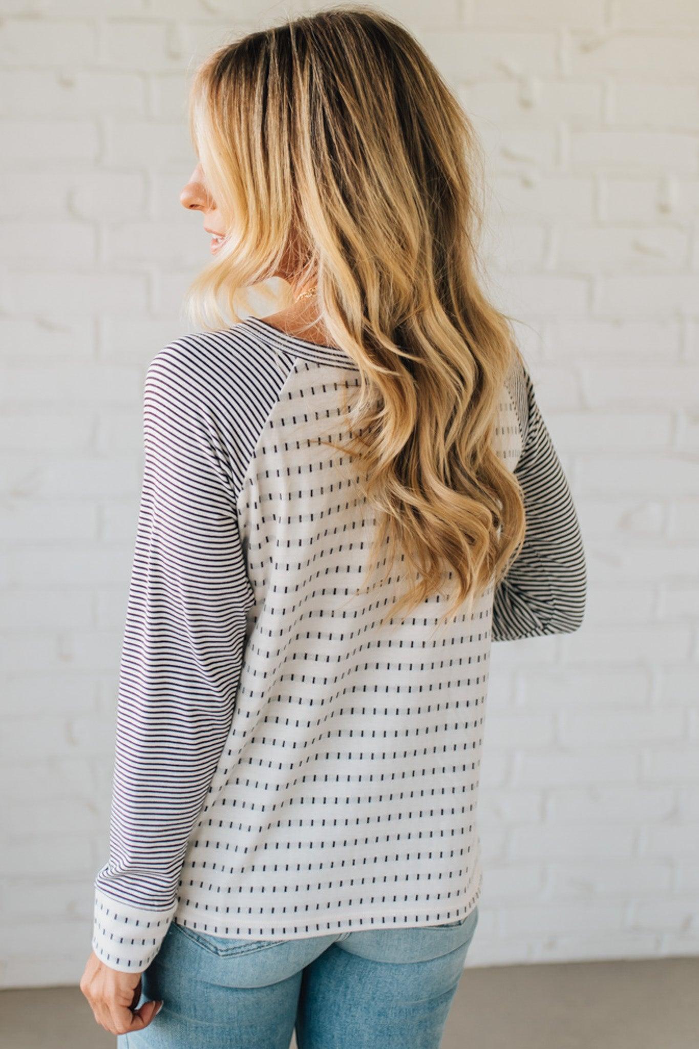 Woman wearing a striped long-sleeve top against a white brick wall.