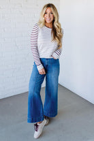 Woman wearing a striped sweater and blue jeans against a white brick wall.
