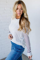 Woman wearing a striped sweater and blue jeans against a white brick wall.