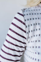 Close-up of a sweater with striped and patterned sleeves against a neutral background