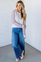 Woman wearing a striped sweater and blue jeans against a white brick wall.