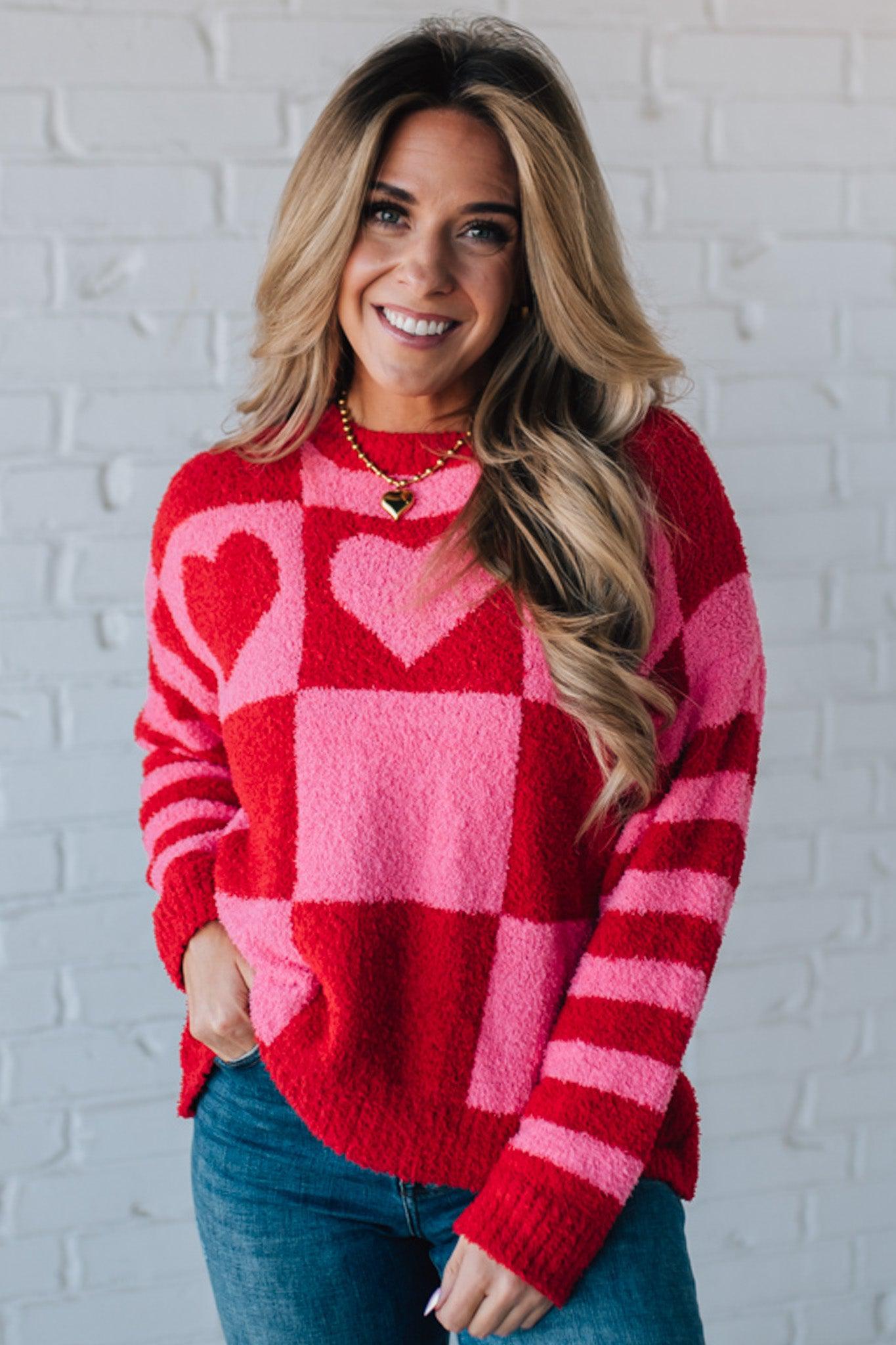 blonde girl modeling a plush valentine sweater with a pink and red checker pattern and striped sleeve