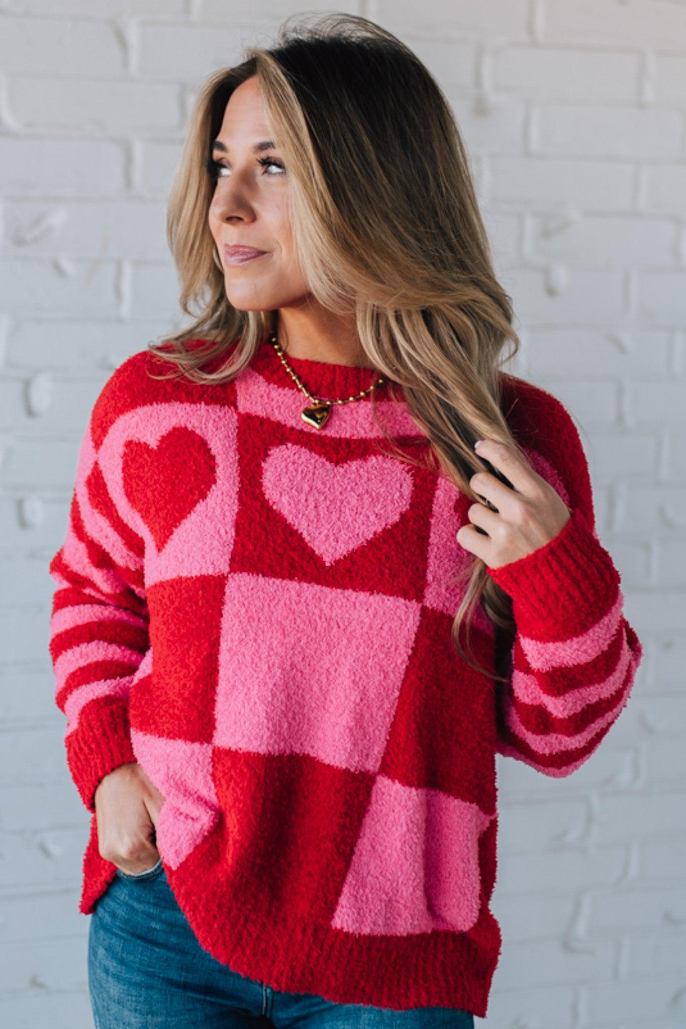 blonde girl modeling a plush valentine sweater with a pink and red checker pattern and striped sleeve