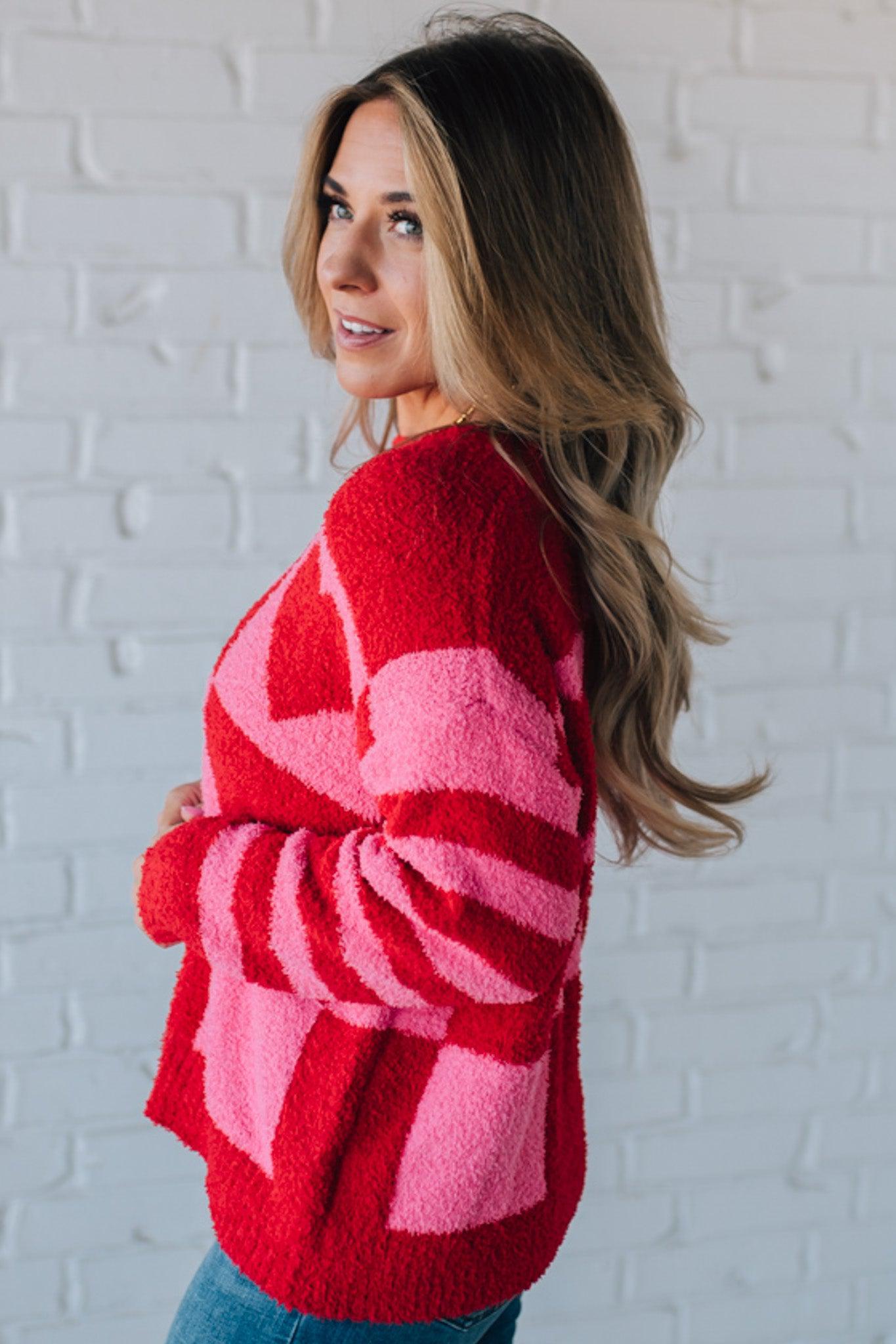 blonde girl modeling a plush valentine sweater with a pink and red checker pattern and striped sleeve