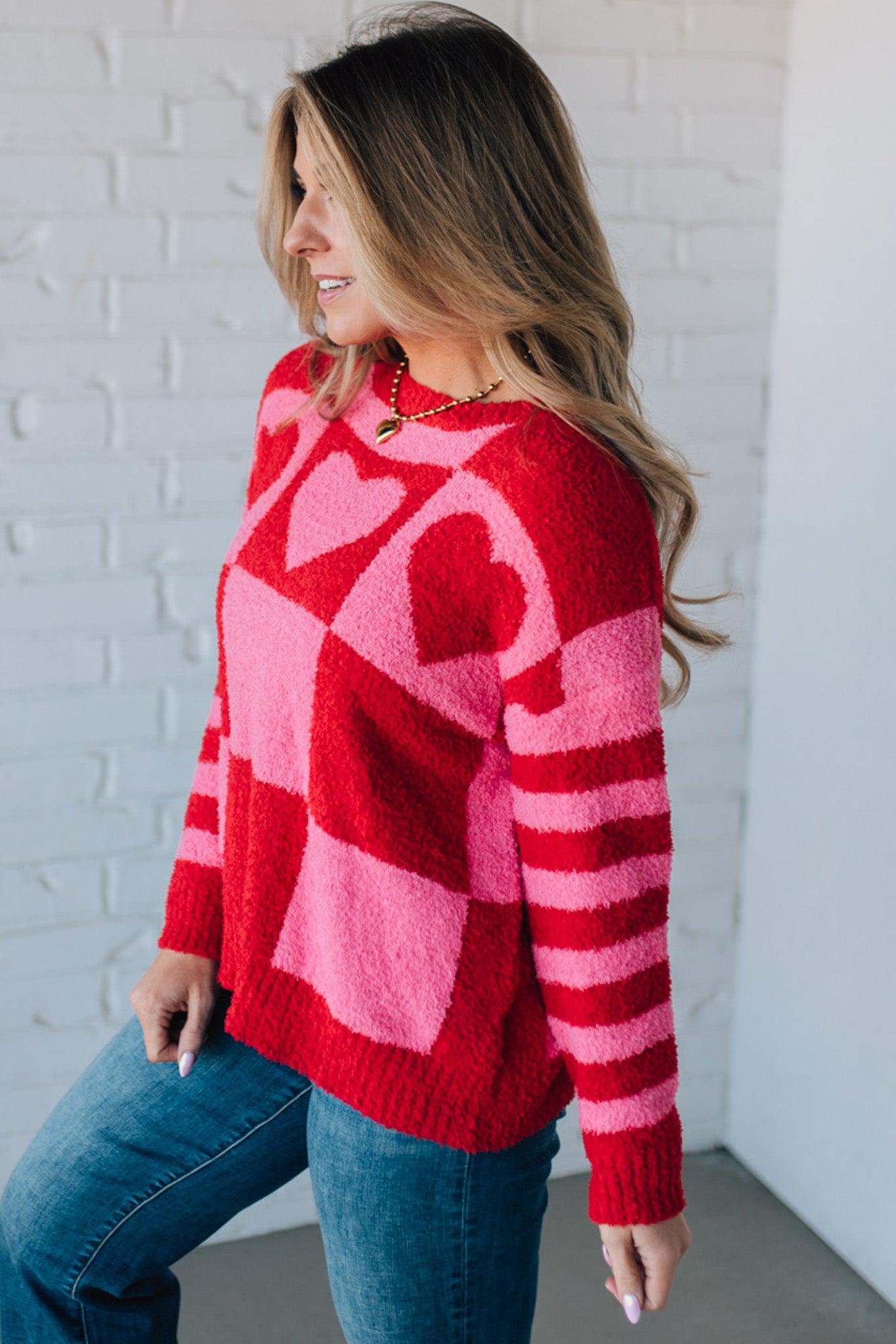 blonde girl modeling a plush valentine sweater with a pink and red checker pattern and striped sleeve