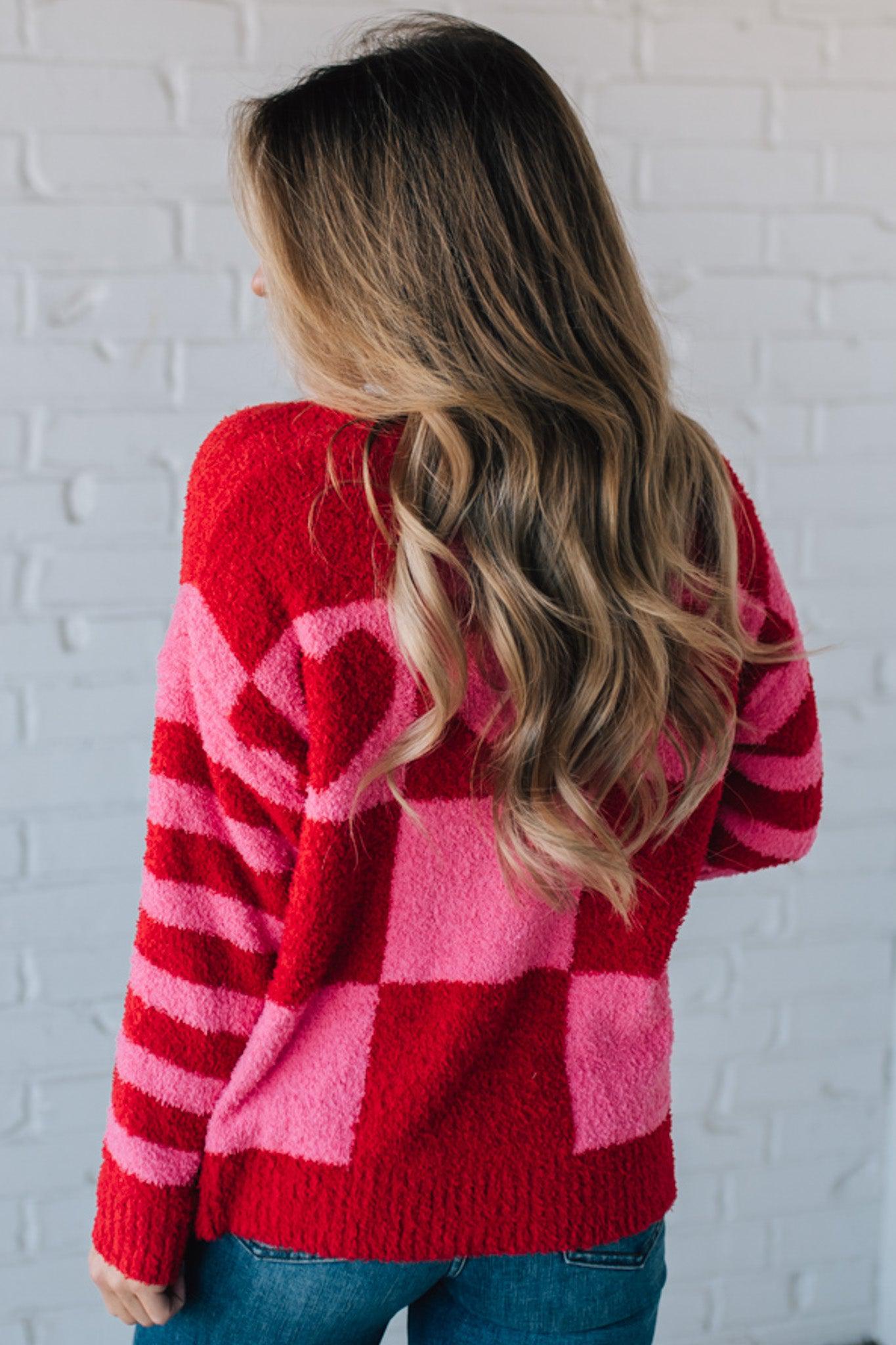 blonde girl modeling a plush valentine sweater with a pink and red checker pattern and striped sleeve