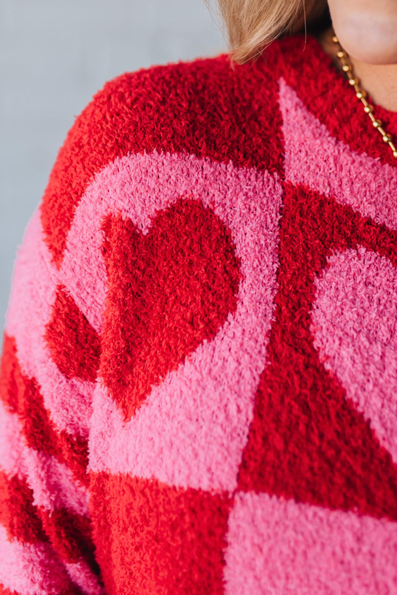 blonde girl modeling a plush valentine sweater with a pink and red checker pattern and striped sleeve