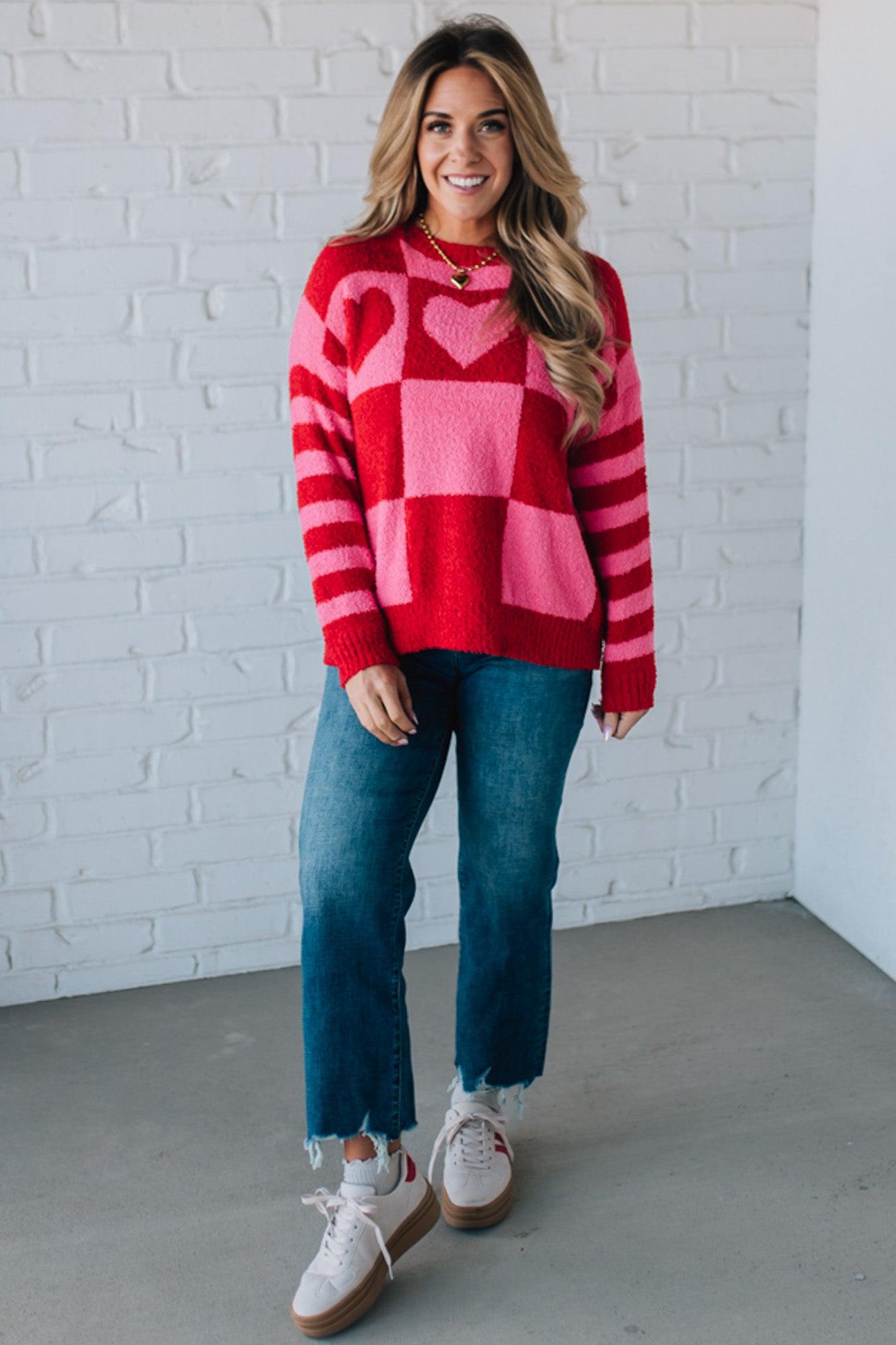 blonde girl modeling a plush valentine sweater with a pink and red checker pattern and striped sleeve