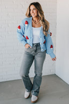 Light blue knit cardigan with charming red and white mushroom appliques on the sleeves and body, on a blonde woman.