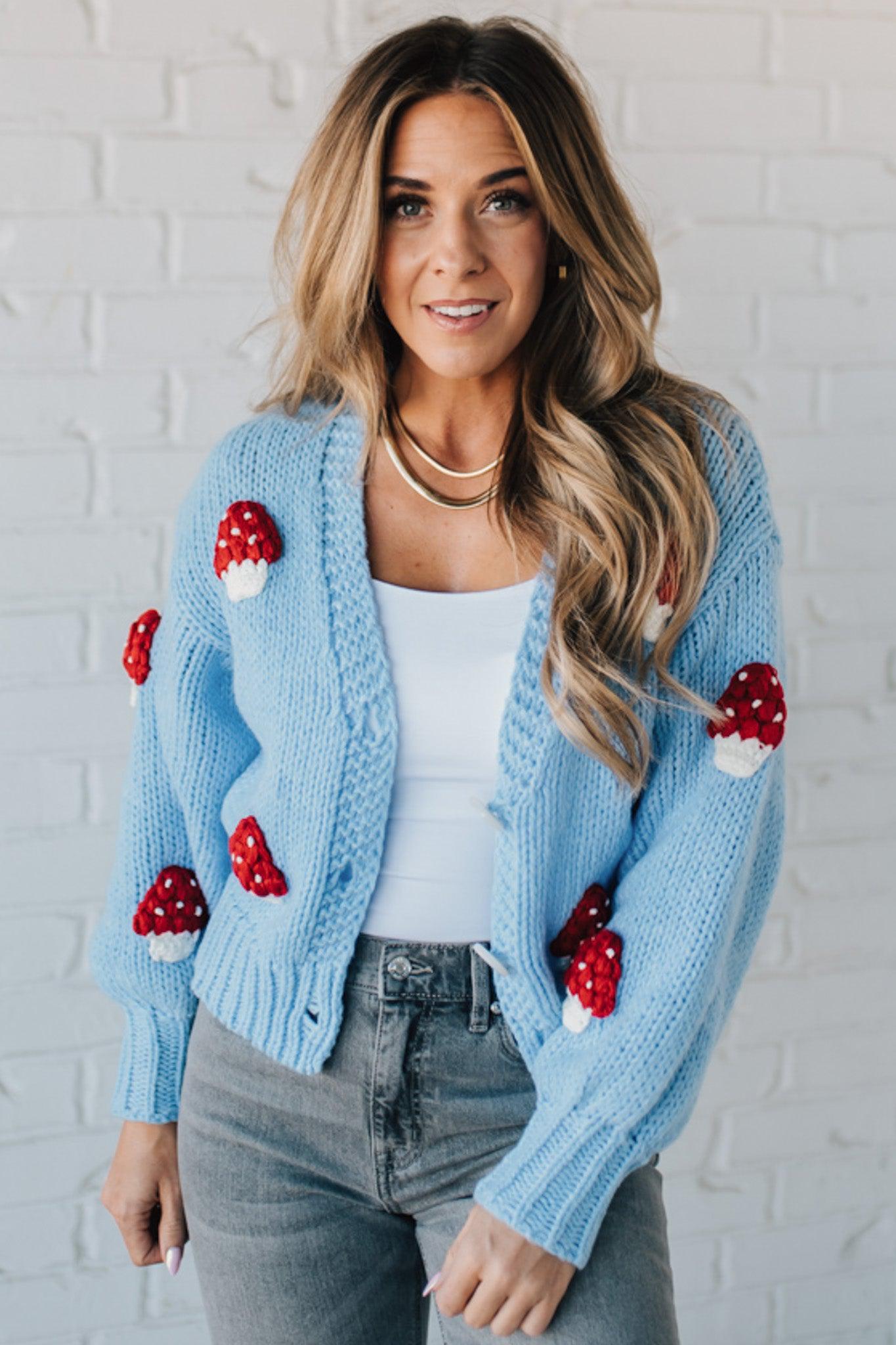 Light blue knit cardigan with charming red and white mushroom appliques on the sleeves and body, on a blonde woman.