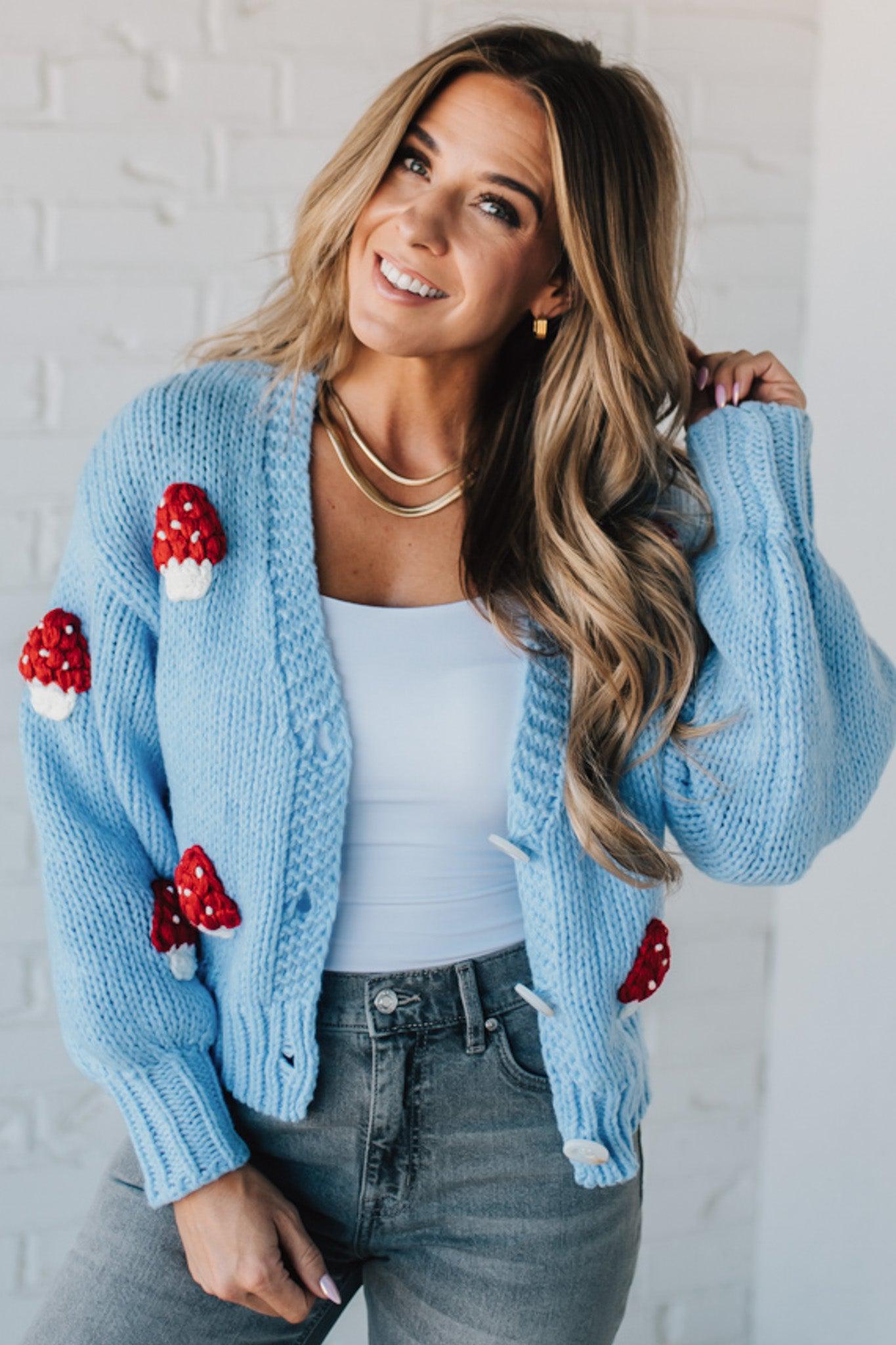 Light blue knit cardigan with charming red and white mushroom appliques on the sleeves and body, on a blonde woman.