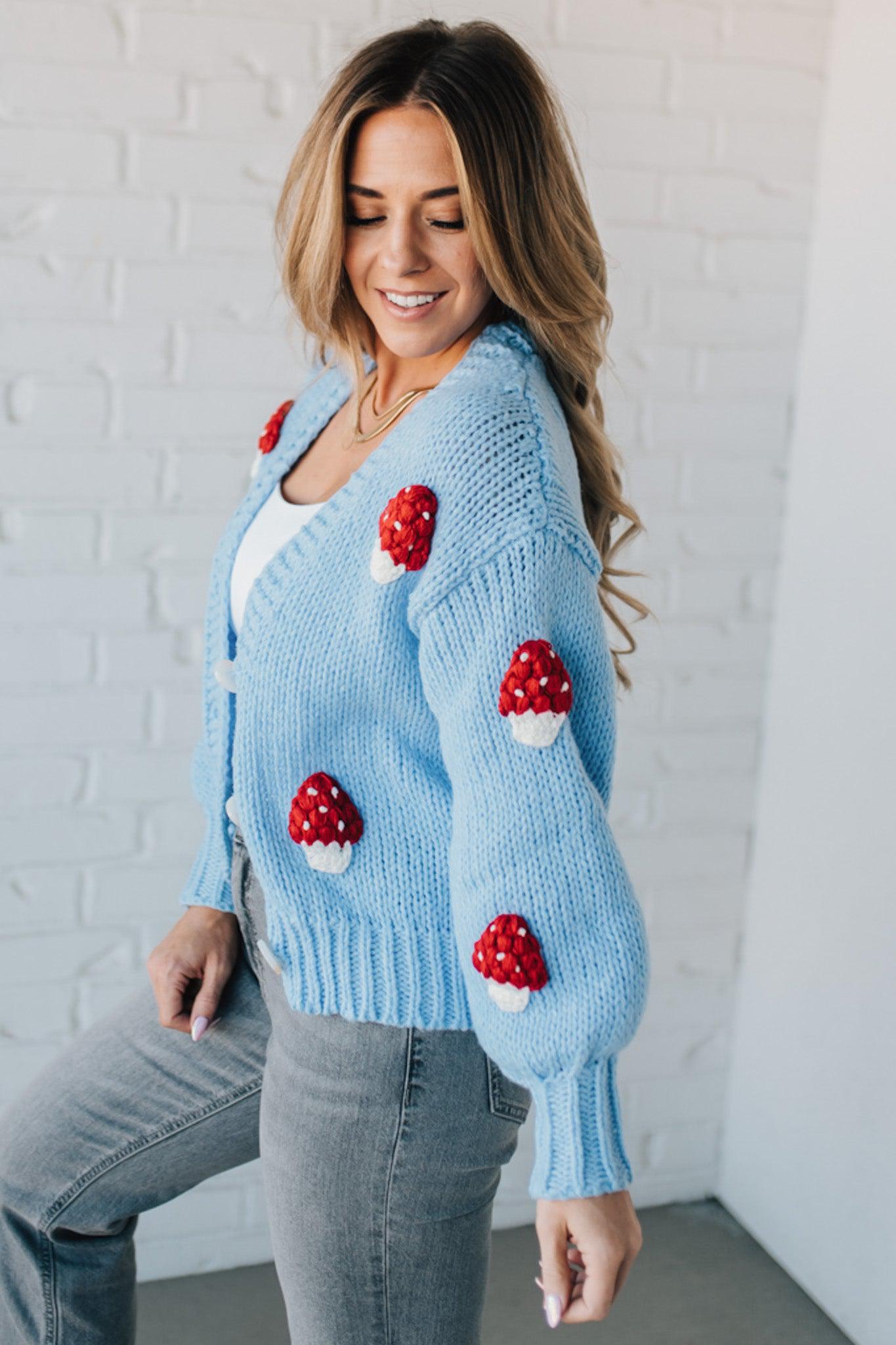 Light blue knit cardigan with charming red and white mushroom appliques on the sleeves and body, on a blonde woman.