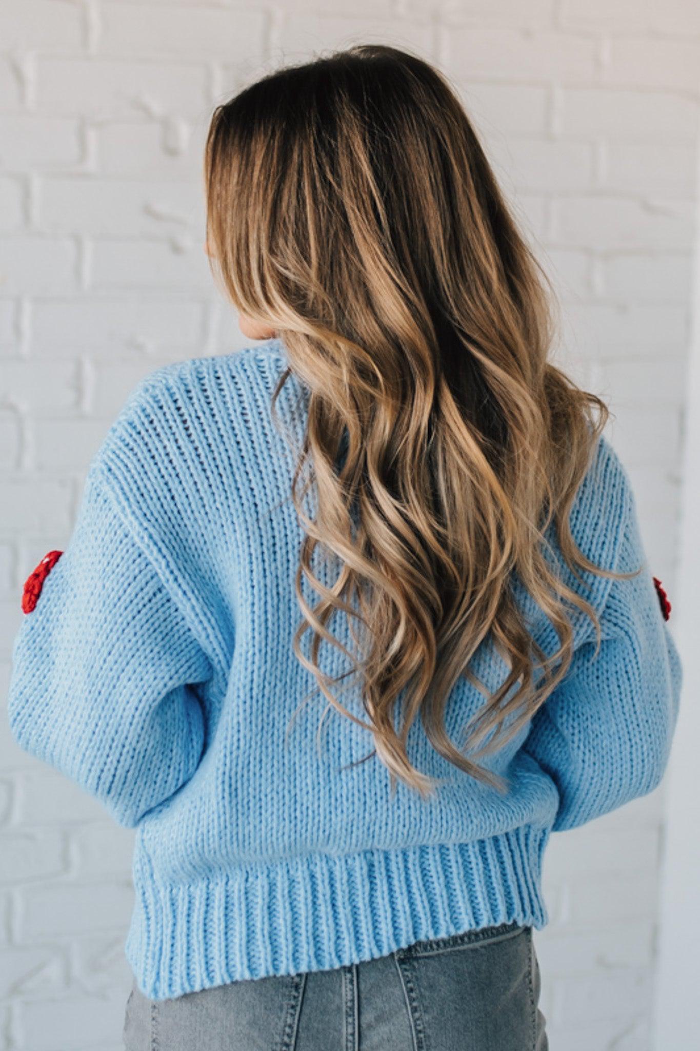 Light blue knit cardigan with charming red and white mushroom appliques on the sleeves and body, on a blonde woman.