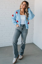 Light blue knit cardigan with charming red and white mushroom appliques on the sleeves and body, on a blonde woman.