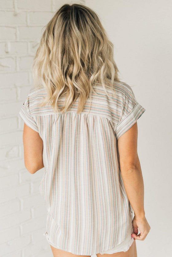 Woman wearing a short sleeve button down top with slim stripes in muted fall toned colors.