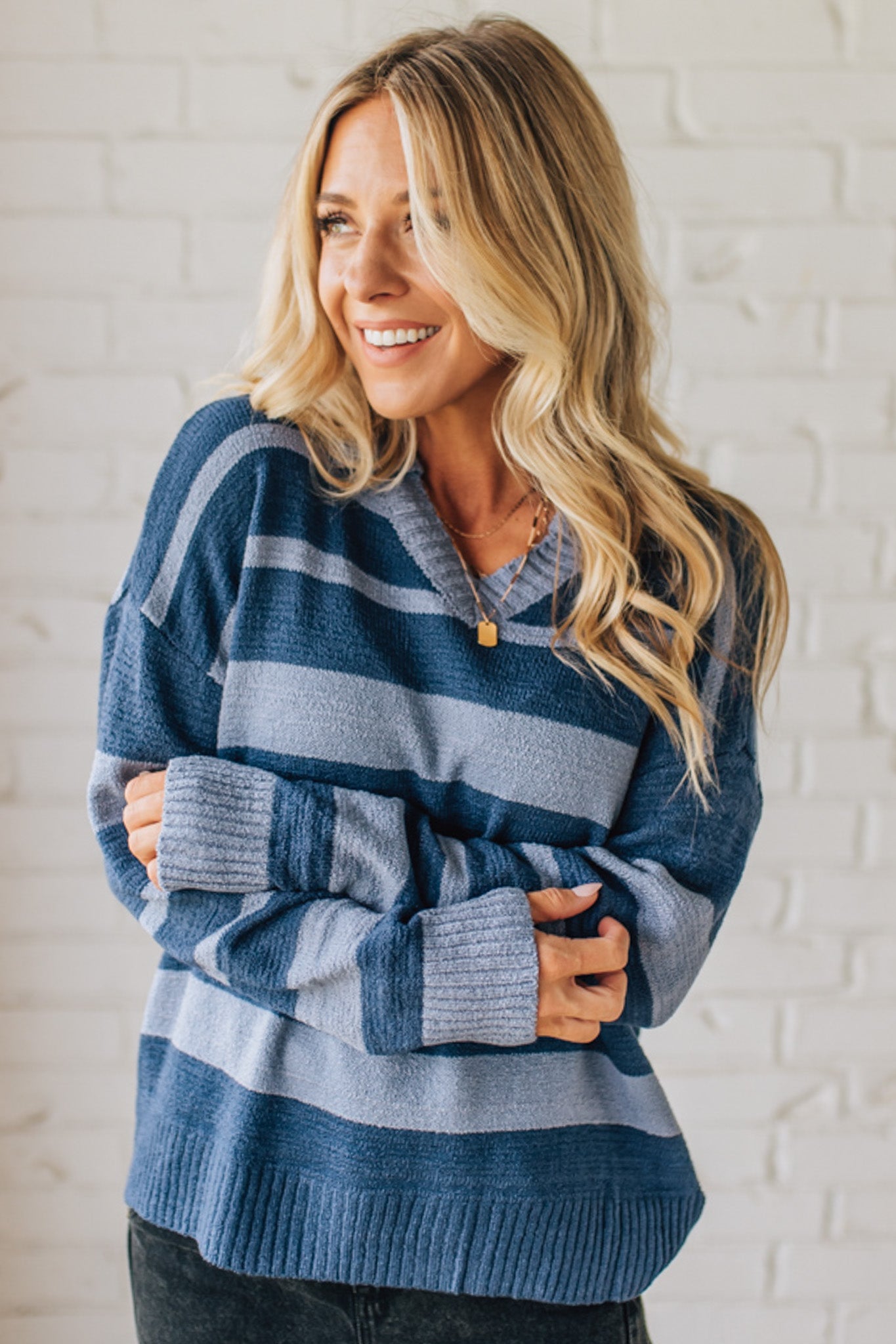 Woman wearing a blue striped sweater against a white brick wall