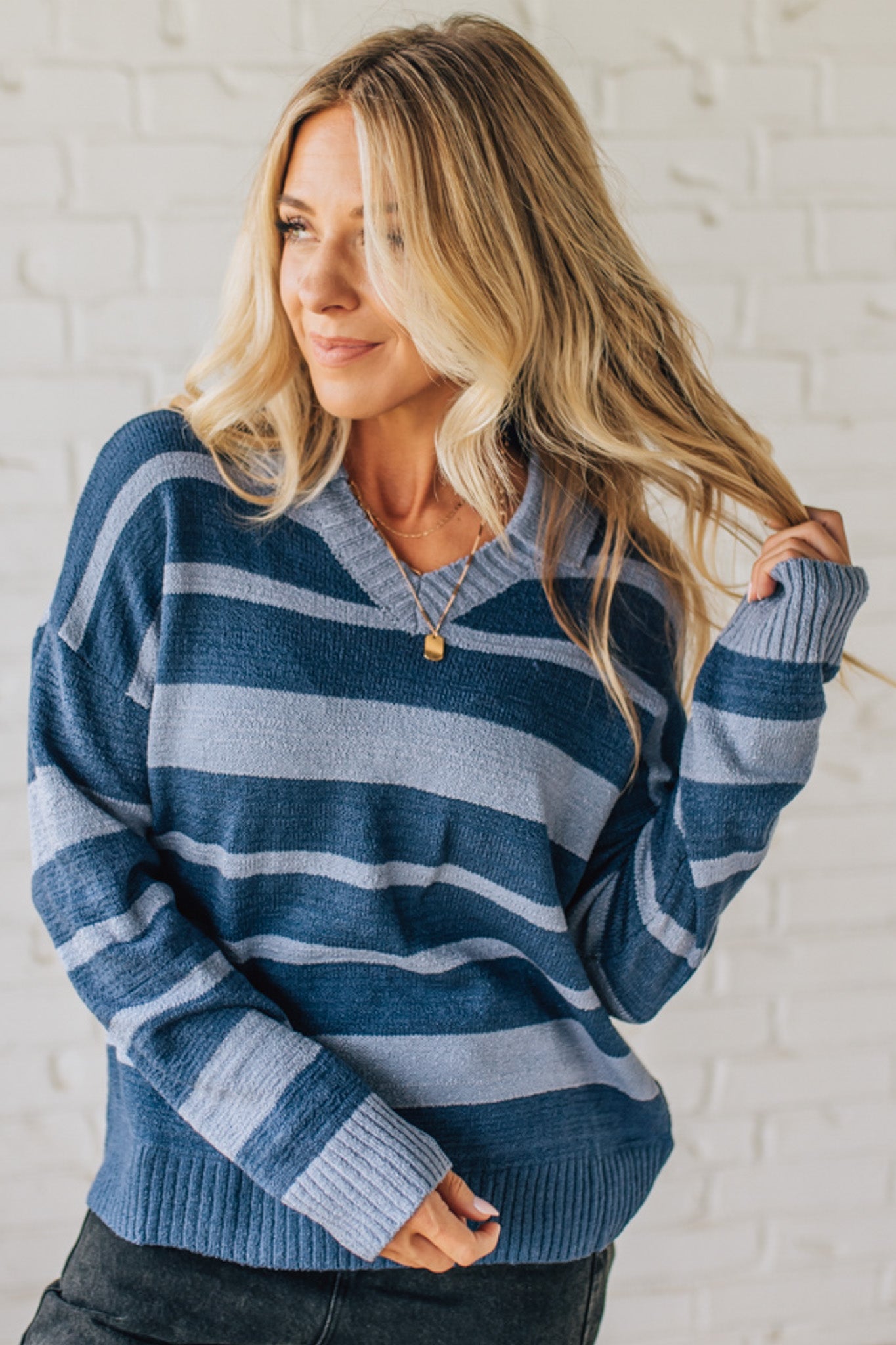 Woman wearing a blue and light blue striped sweater against a white brick wall.