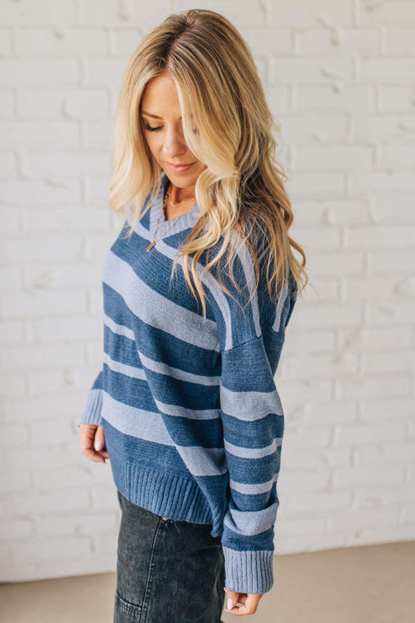Woman wearing a blue and light blue striped sweater against a white brick wall.