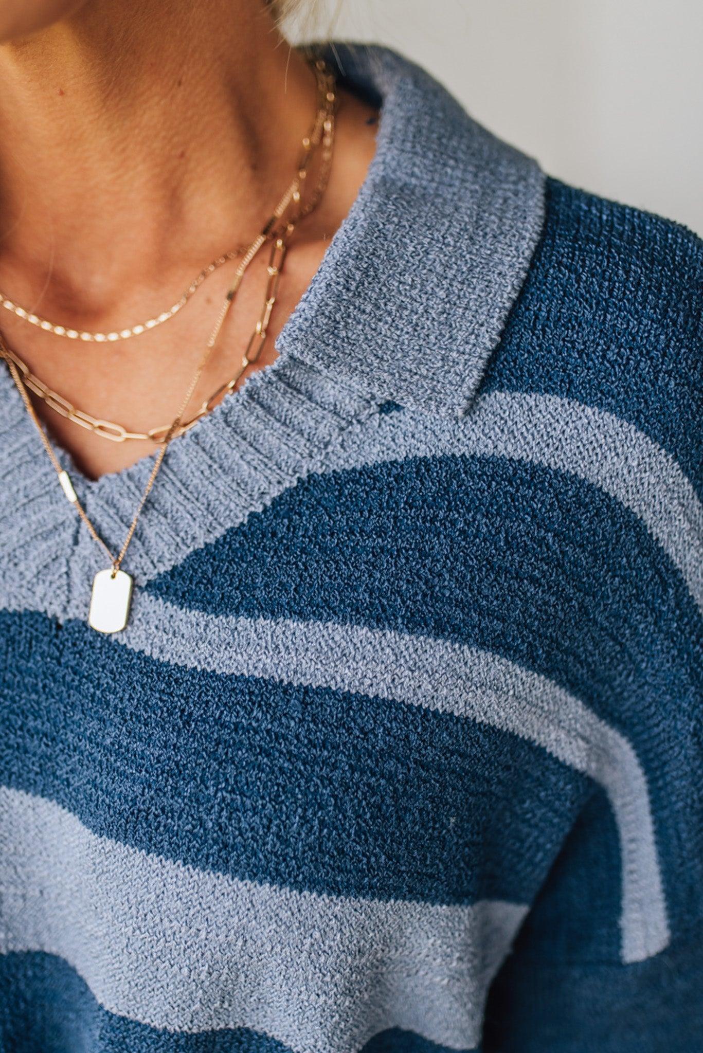 Close-up of a person wearing a blue and light blue striped sweater with layered necklaces.