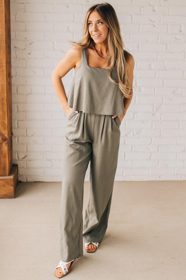 Blonde woman wearing a tank style olive linen blend wide leg jumpsuit with wide leg, pockets, and a square neckline.