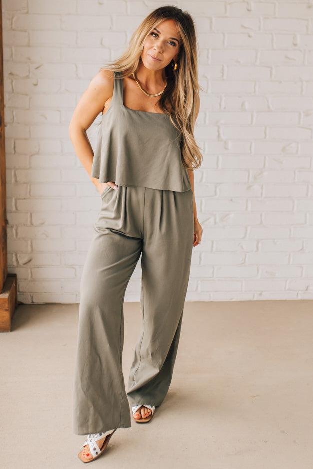 Blonde woman wearing a tank style olive linen blend wide leg jumpsuit with wide leg, pockets, and a square neckline.