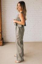 Blonde woman wearing a tank style olive linen blend wide leg jumpsuit with wide leg, pockets, and a square neckline.