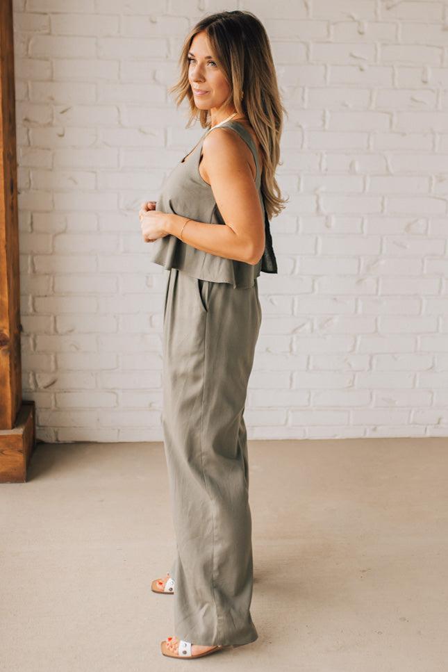 Blonde woman wearing a tank style olive linen blend wide leg jumpsuit with wide leg, pockets, and a square neckline.