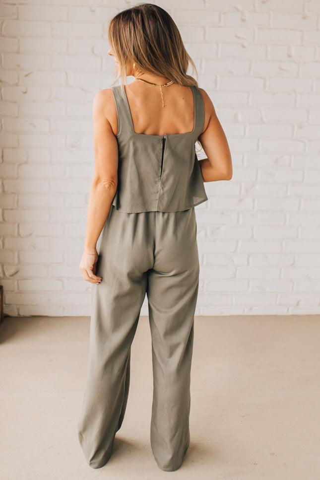 Blonde woman wearing a tank style olive linen blend wide leg jumpsuit with wide leg, pockets, and a square neckline.