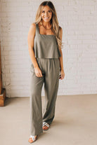 Blonde woman wearing a tank style olive linen blend wide leg jumpsuit with wide leg, pockets, and a square neckline.