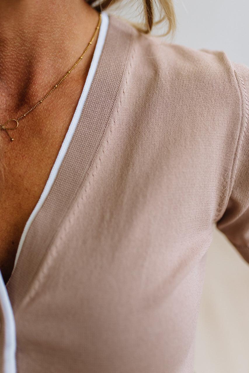 Close-up of a person wearing a soft blush-beige knit top with a white inner layer visible at the neckline, along with a delicate gold chain necklace.