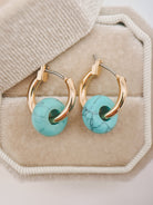 Gold hoop earrings with round turquoise beads, displayed on a beige jewelry box.