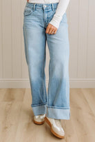 Person wearing light blue jeans and white shoes on a wooden floor.