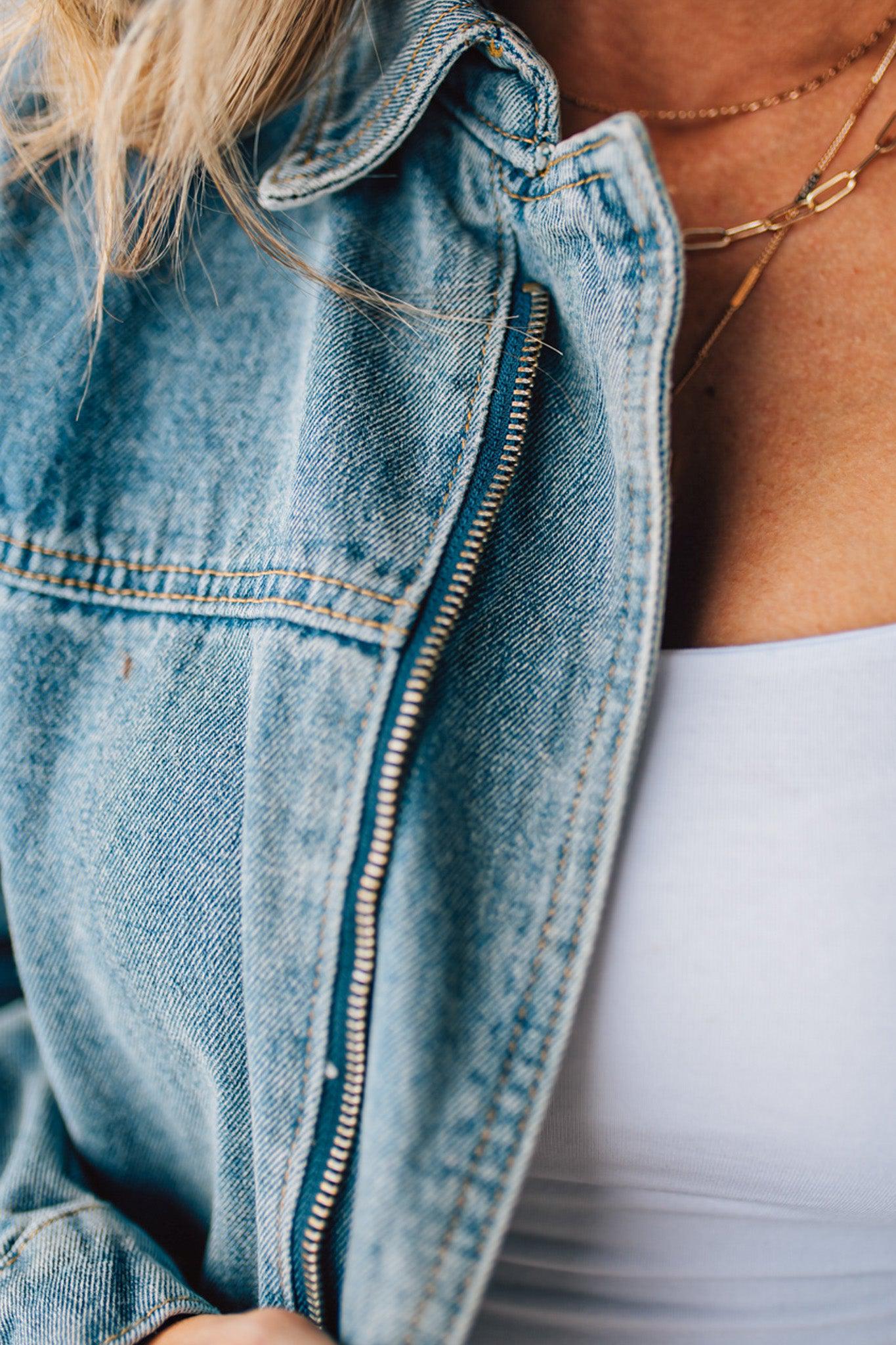 Blonde woman wearing a medium wash zip front denim moto jacket.