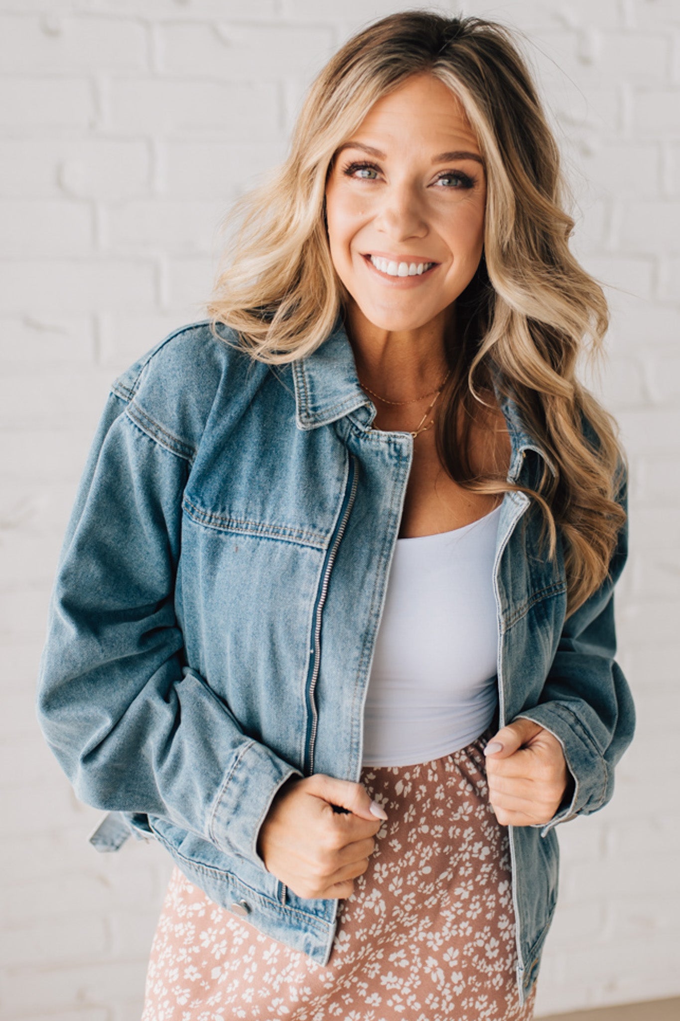 Blonde woman wearing a medium wash zip front denim moto jacket.