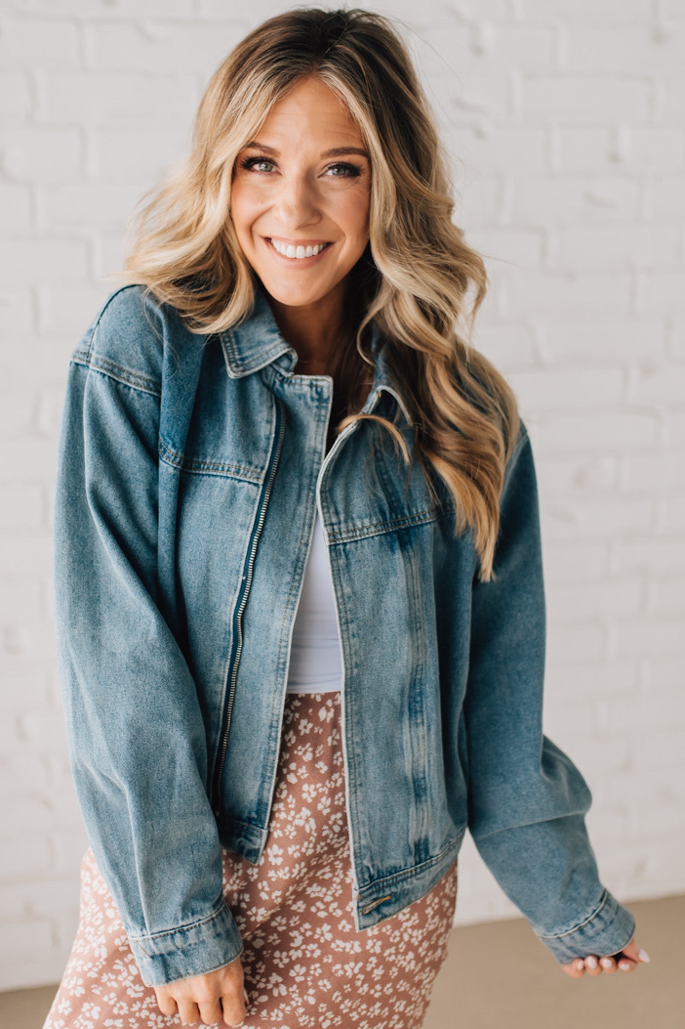 Blonde woman wearing a medium wash zip front denim moto jacket.