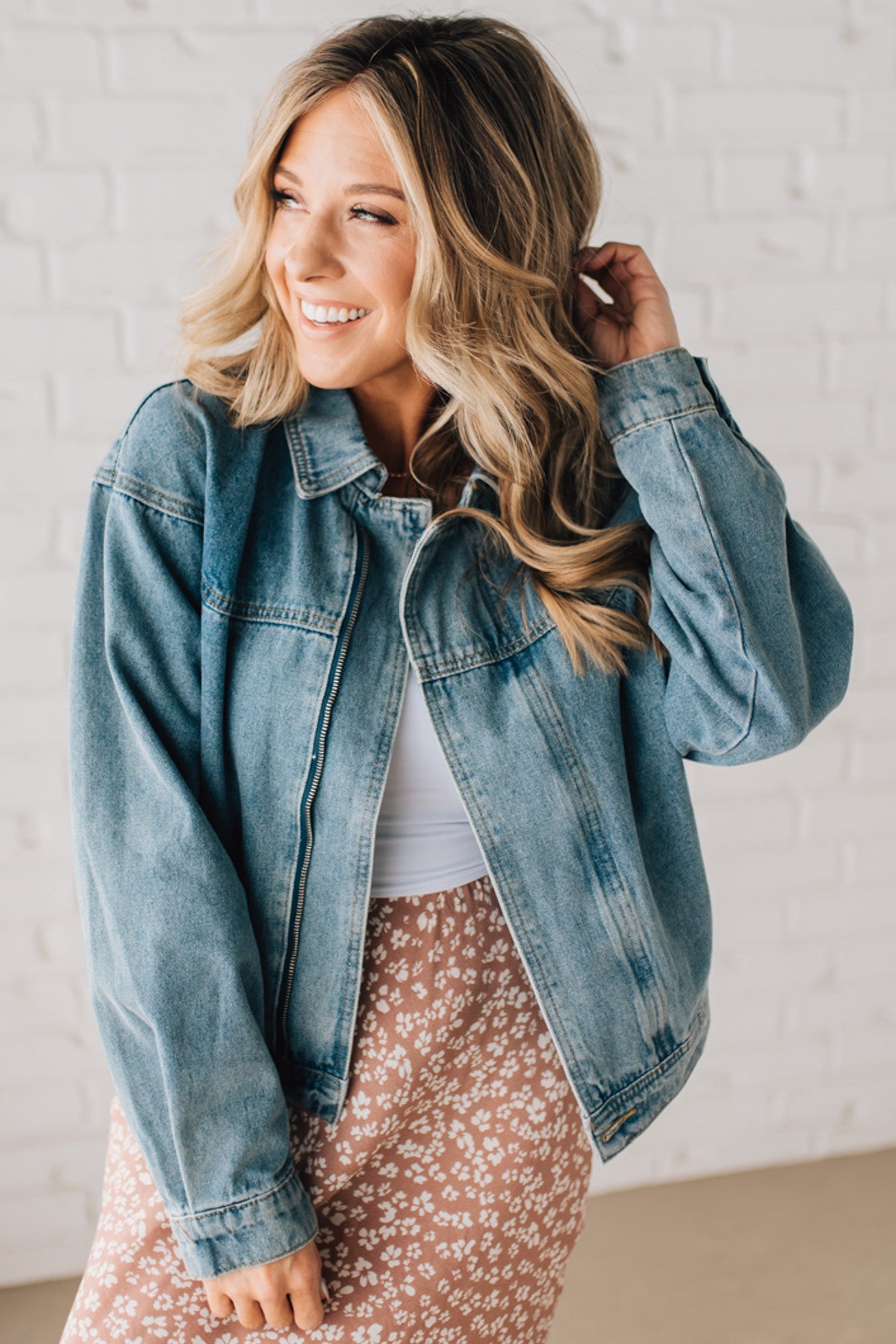 Blonde woman wearing a medium wash zip front denim moto jacket.