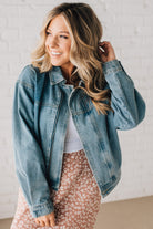 Blonde woman wearing a medium wash zip front denim moto jacket.