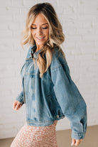 Blonde woman wearing a medium wash zip front denim moto jacket.