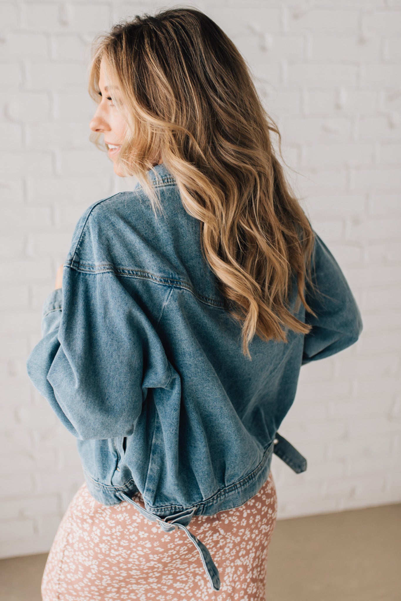 Blonde woman wearing a medium wash zip front denim moto jacket.