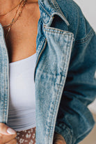 Blonde woman wearing a medium wash zip front denim moto jacket.