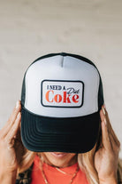 Blonde woman wearing a black and white trucker hat with a "NEED A DIET COKE" patch.