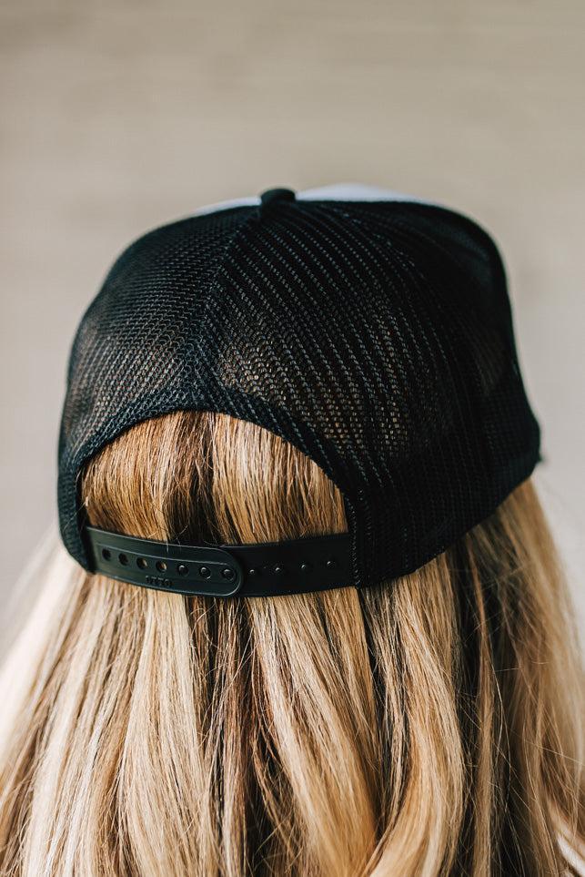 Blonde woman wearing a black and white trucker hat with a "NEED A DIET COKE" patch.