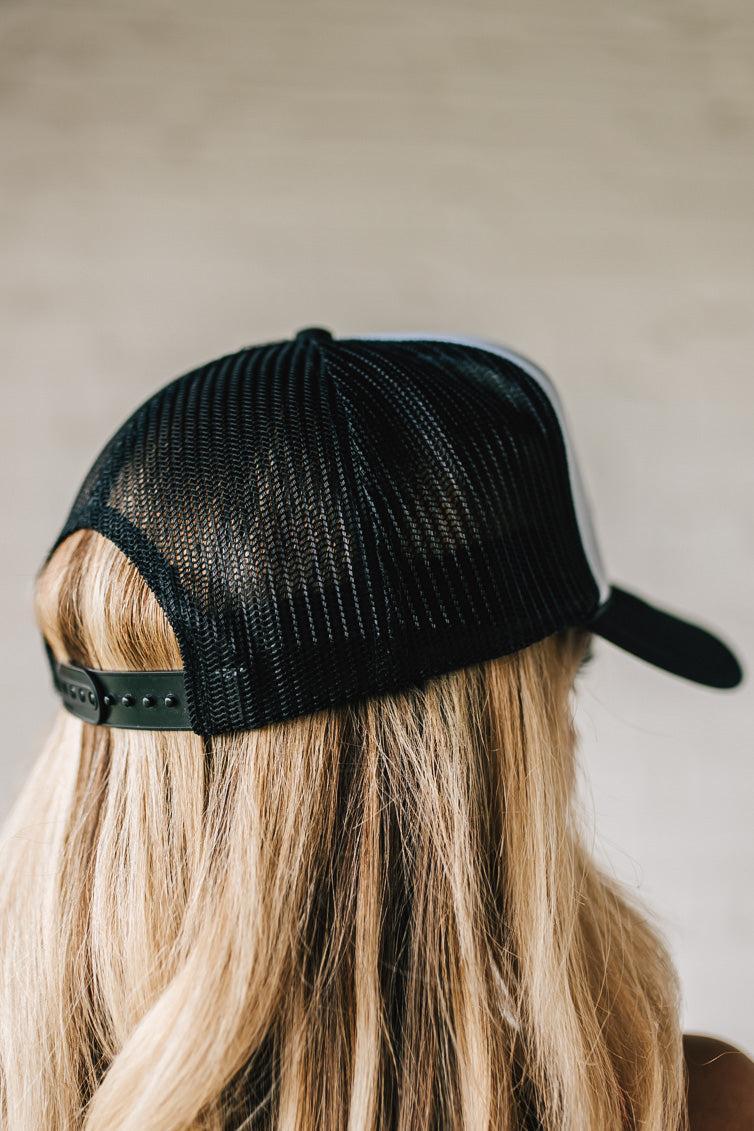 Blonde woman wearing a black and white trucker hat with a "NEED A DIET COKE" patch.