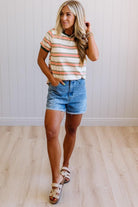 Woman wearing a striped shirt and denim shorts standing on a wooden floor.