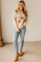 Woman wearing a floral sweater and jeans standing against a white brick wall.